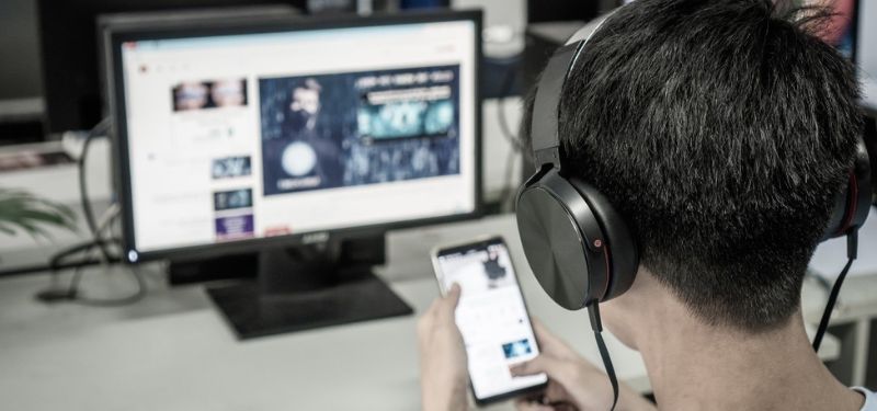 man at his computer looking at mobile device 