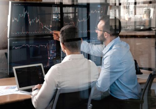 Two men at work sitting side by side analyzing  data on monitors in front of them 